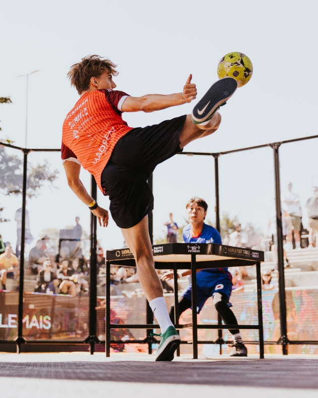 Two athletes playing Foot Table around a table inside an enclosed arena